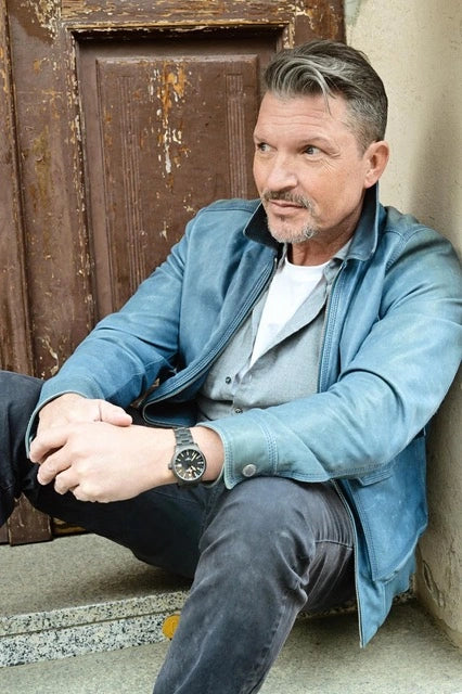 Hardy Krüger im blauen Hemd vor einer Holztür